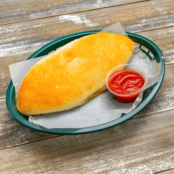 Golden-brown calzone in a green basket with a side of red marinara sauce on a wooden table.