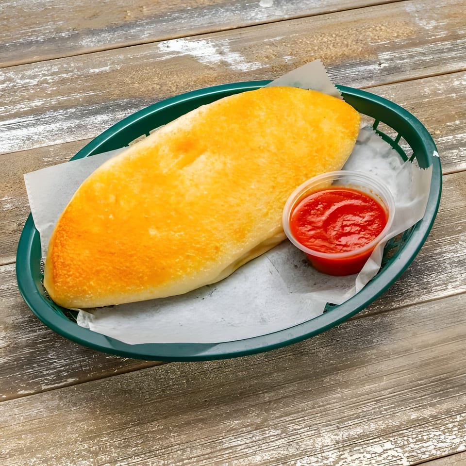 Golden-brown calzone in a green basket with a side of red marinara sauce on a wooden table.