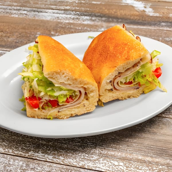 Two halves of a deli sandwich with turkey, lettuce, and tomatoes on a white plate.
