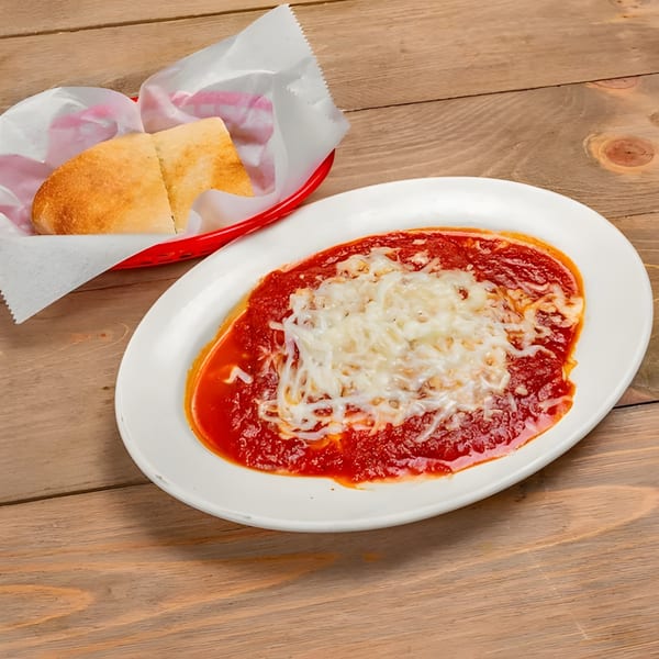 Baked ziti with melted mozzarella cheese and marinara sauce, served with bread in a red basket.