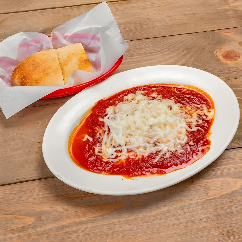 Baked ziti with melted mozzarella cheese and marinara sauce, served with bread in a red basket.