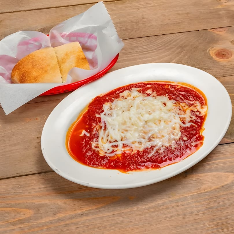 Baked ziti with melted mozzarella cheese and marinara sauce, served with bread in a red basket.