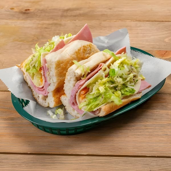 Two Roma Pizza Restaurant subs, filled with ham, cheese, and shredded lettuce, in a green basket.