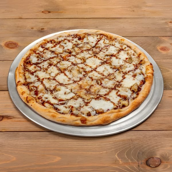 A whole Roma Pizza Restaurant BBQ chicken pizza with white cheese and sauce drizzle on a wooden table.