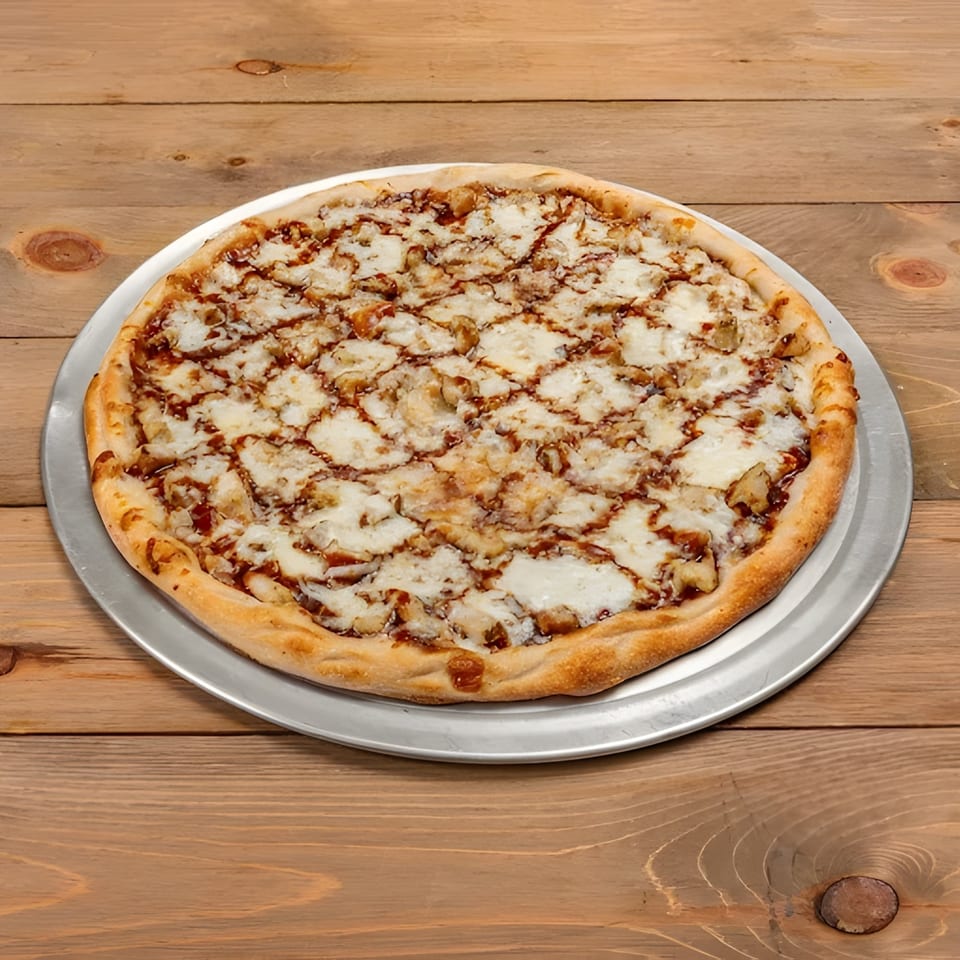 A whole Roma Pizza Restaurant BBQ chicken pizza with white cheese and sauce drizzle on a wooden table.